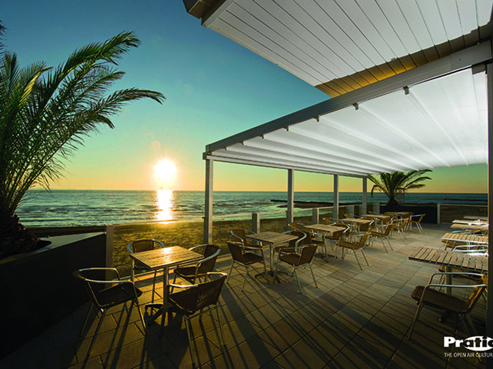 pergola over an oceanfront seating area with palm trees sand and a sunset